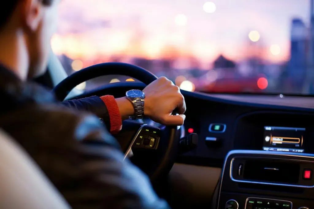 Driver's hands on the steering wheel with city lights through the windshield